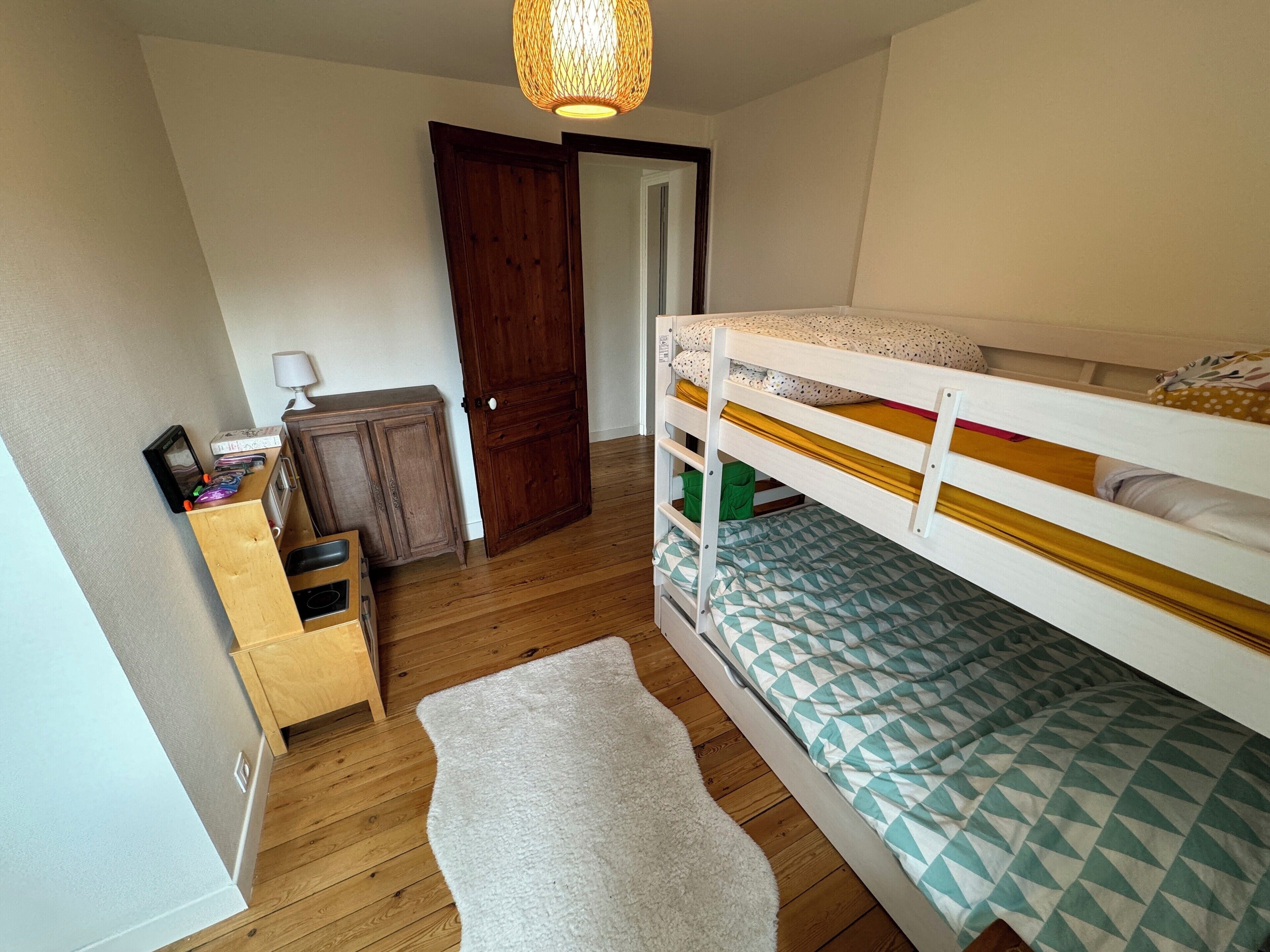 A bedroom with a bunk bed, wooden dresser, and a door leading to another room.