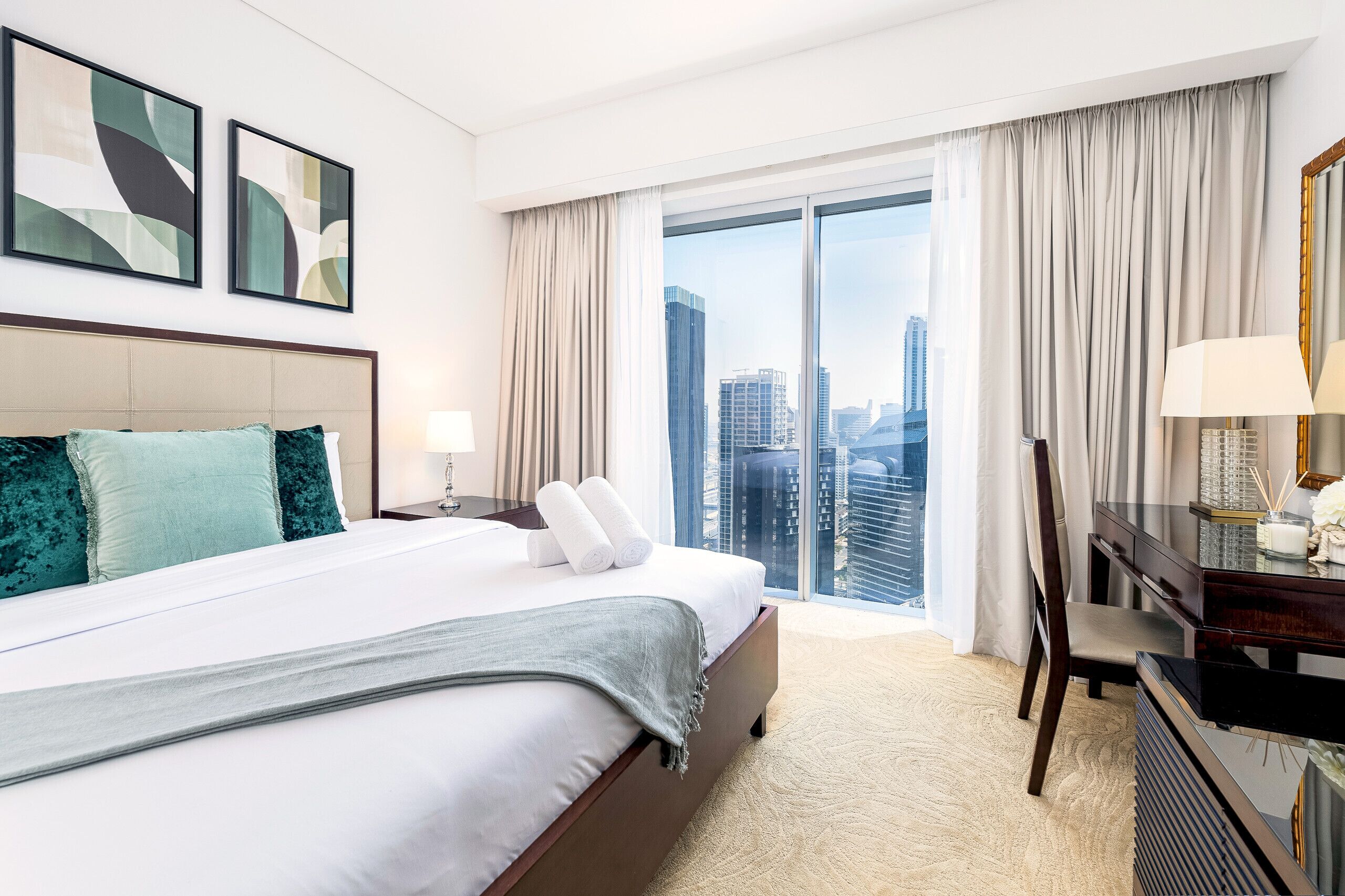 Ein Hotelzimmer mit einem großen Bett, einem Schreibtisch mit Lampe, einem Sessel und Blick auf die Stadt durch ein großes Fenster.