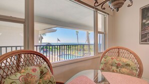 Ein Zimmer mit Blick auf einen Pool und Palmen, ausgestattet mit Korbmöbeln und einem Glastisch.