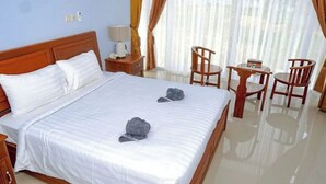 A hotel room with a large bed, a bedside table with a lamp, a small table with chairs, and a view of the outdoors through sheer curtains. - Sansapore Pacific Park Resort (Sausapor)