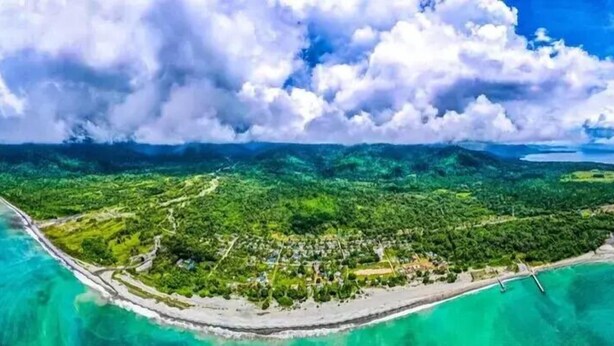 An aerial view of a coastal area with a beach, dense greenery, and a clear sky. - Sansapore Pacific Park Resort (Sausapor)