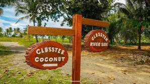 A wooden signpost with two circular signs indicating directions to 'Cluster Coconut' and 'Gluster River Side'. - Sansapore Pacific Park Resort (Sausapor)