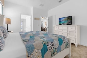 A bedroom with a bed, a television on a dresser, and a door leading to another room.