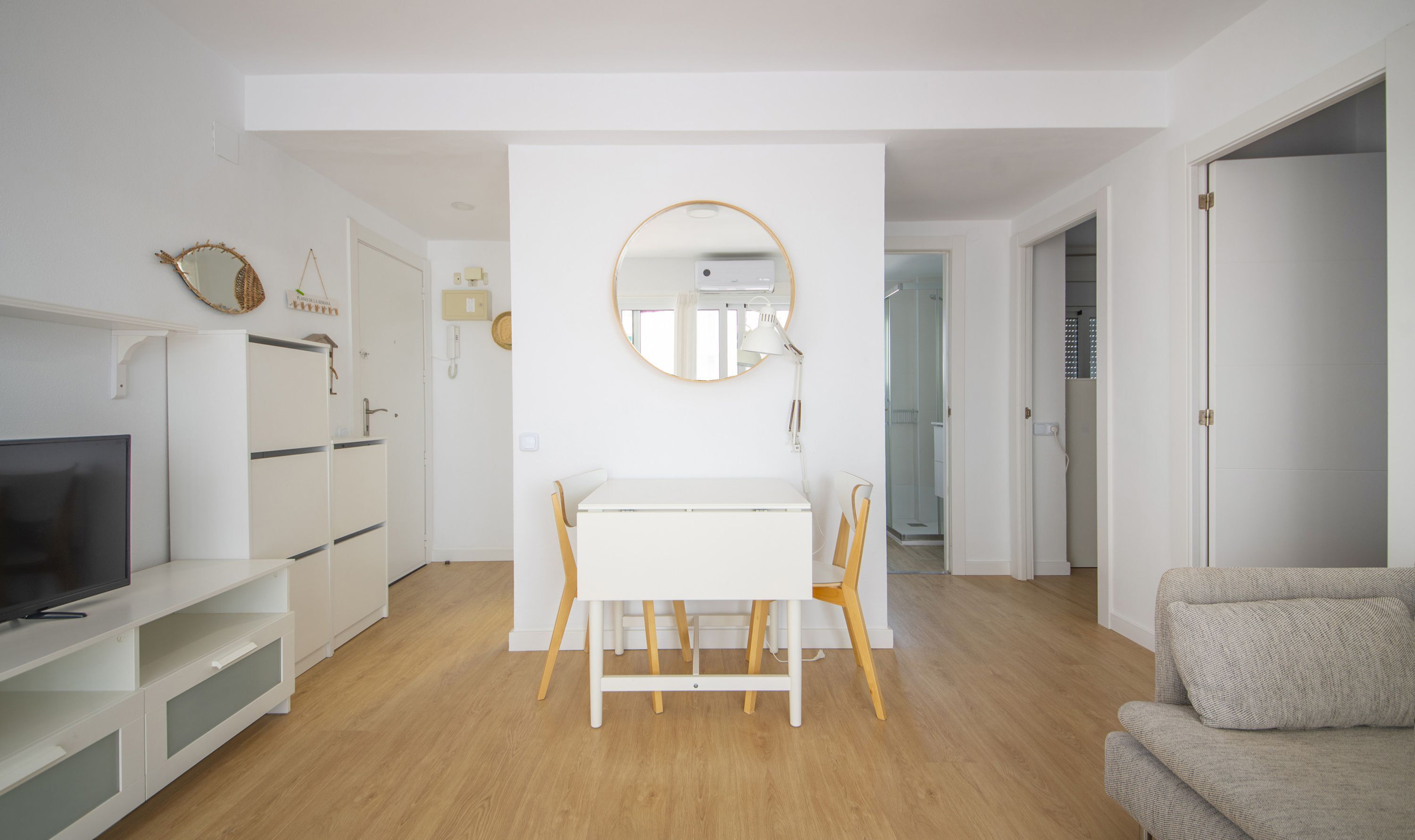 A modern living room with a TV, white cabinets, a dining table, and a round mirror.