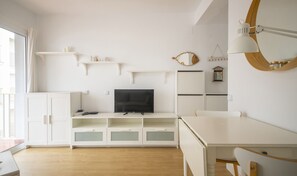 A modern, minimalist living room with a flat-screen TV, white cabinetry, and a dining area. - R156 - Apartamento Ganna (Calafell)