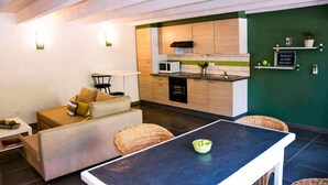Une cuisine moderne équipée d’un four à micro-ondes, d’une cuisinière et agrémentée d’un mur vert. On y trouve également un coin repas avec une table et des chaises.