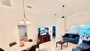 Ein modernes Wohnzimmer mit Essbereich, einer Couch, einem Fernseher und einer Treppe zu einem weiteren Raum.