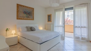 A bedroom with a bed, bedside tables, a nightstand, a lamp, a framed picture on the wall, and a view of the outside through a door. - Sunflowers Home - by Varenna Holidays (Mandello del Lario)