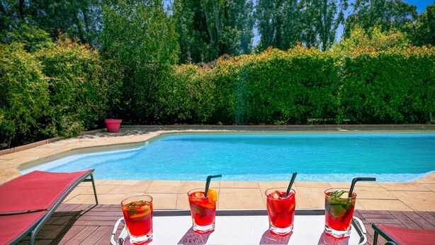 Ein Swimmingpool mit vier Gläsern roter Getränke auf einem Tisch.
