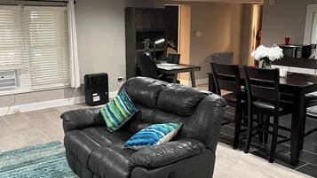 Een moderne woonkamer met een zwarte leren bank, een eettafel met stoelen en een keuken op de achtergrond.