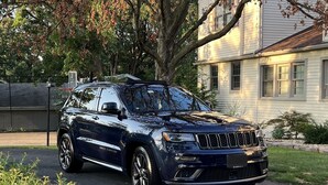 A dark blue Jeep SUV parked in front of a house with a large tree and a well-maintained lawn.