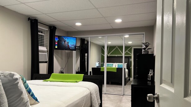 A hotel room with a bed, a TV mounted on the wall, a desk with a chair, and a door.