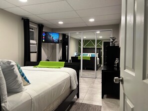 A hotel room with a bed, a TV mounted on the wall, a desk with a chair, and a door. - Cozy Garden Unit 1st flr with private entrance and Turo vehicle available.  (Hickory Hills)