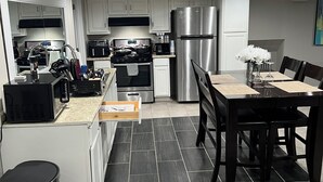 A modern kitchen with white cabinets, stainless steel appliances, and a dining area with a wooden table and chairs.
