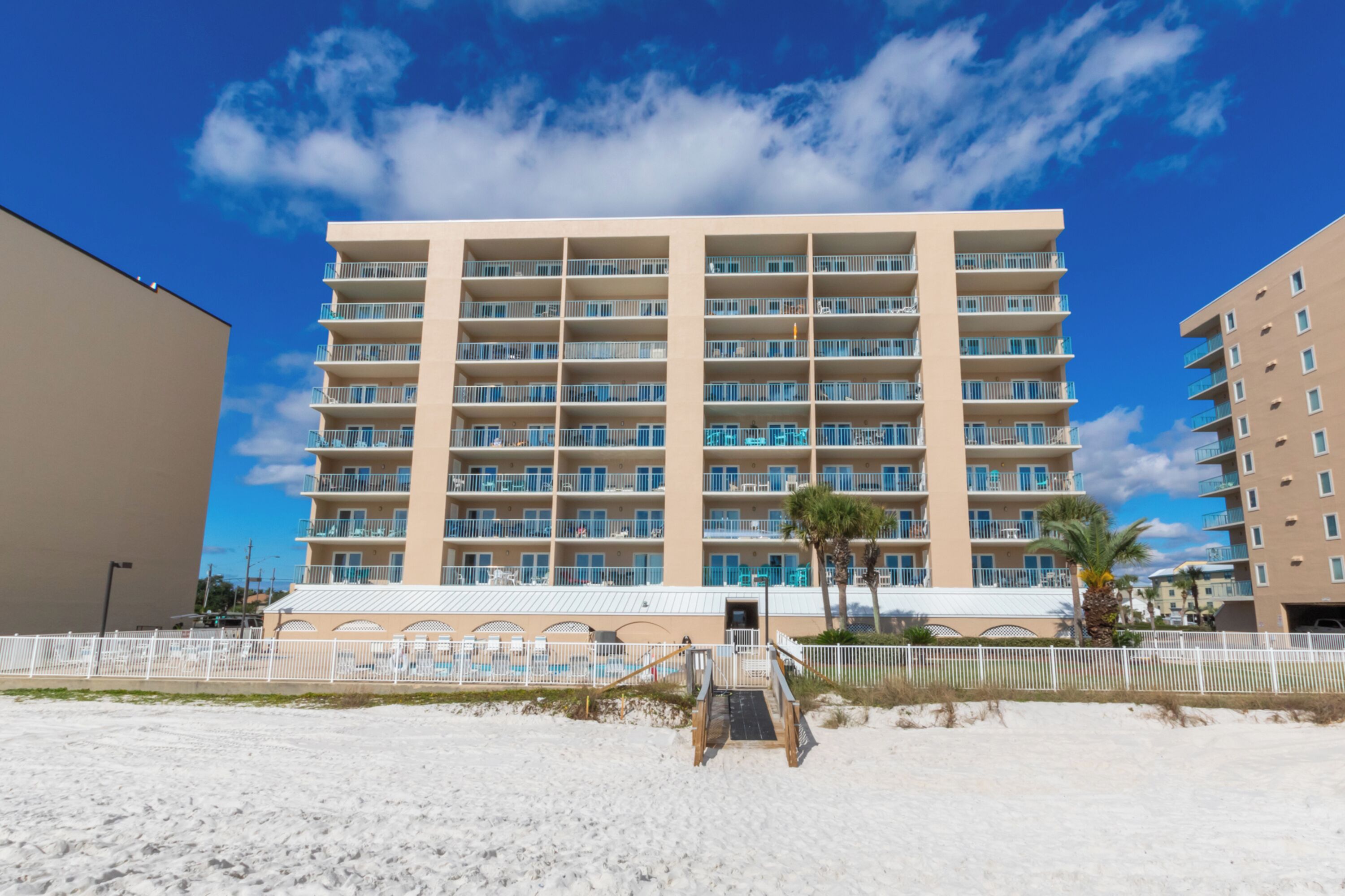 Um hotel com vários andares, fachada plana, varandas e uma praia arenosa em primeiro plano.