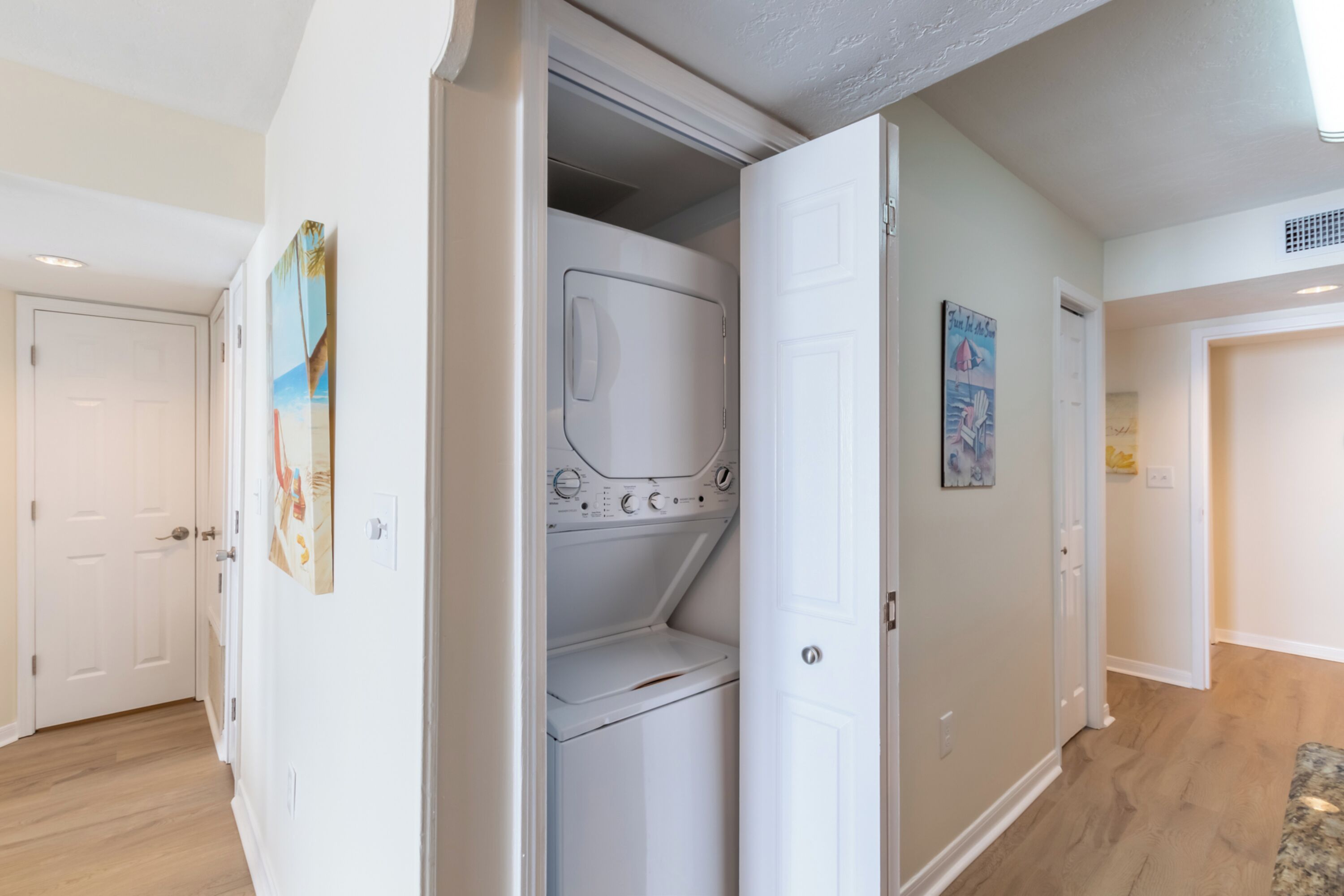 A laundry room with a built-in washer and dryer, a door leading to another room, and a painting on the wall.