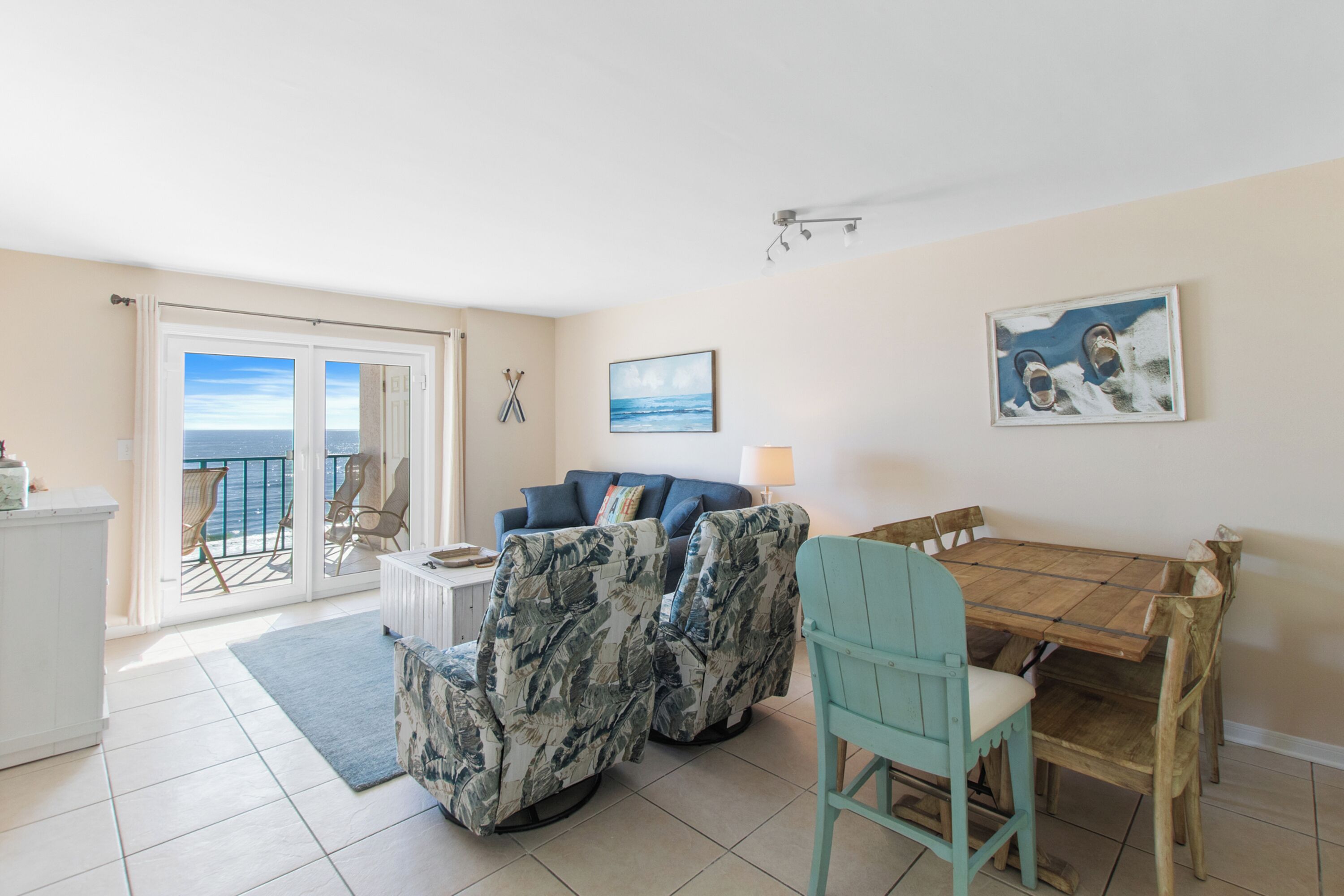 A living room with a sofa, chairs, a dining table, and a view of the ocean through the sliding glass door.