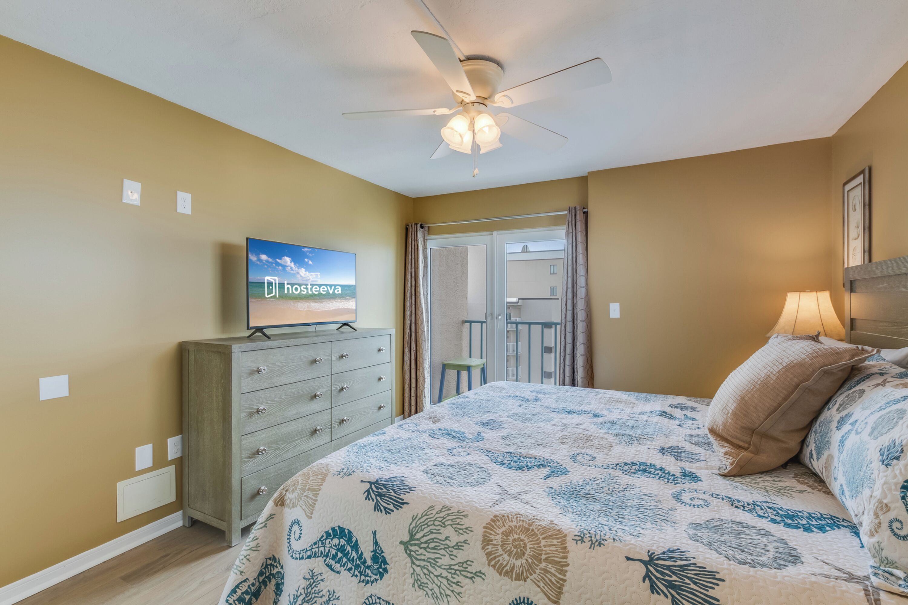 Une chambre d’hôtel avec un lit, un ventilateur de plafond, une télévision et une vue sur l’extérieur.