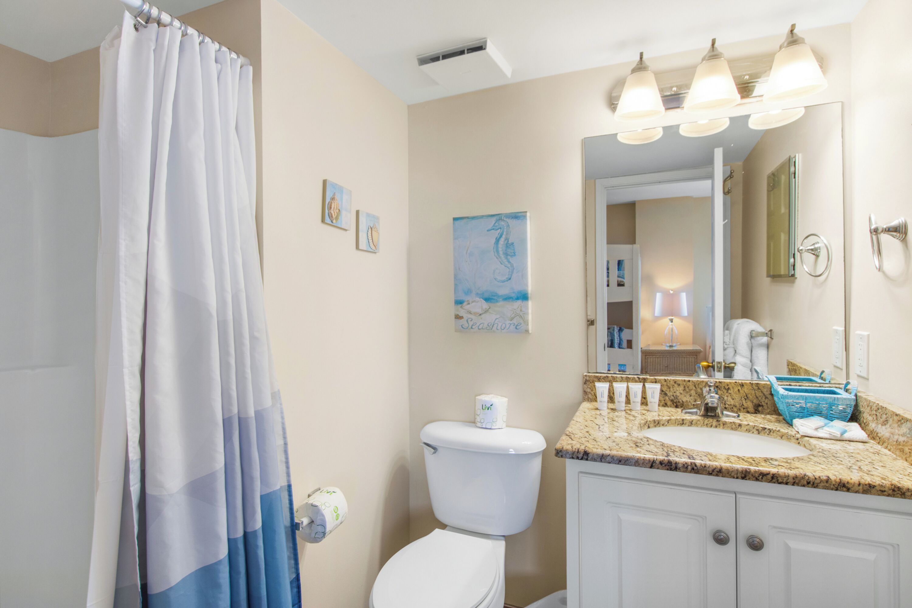 A bathroom with a shower curtain, toilet, sink, and a mirror with lights.