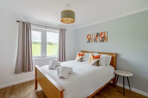 A bedroom with a wooden bed, a small round table, and a view of a green field through the window.