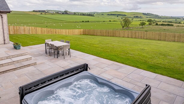 A hot tub on a patio with a view of a grassy field and hills. - Berryrigg Cottage -  a cottage that sleeps 6 guests in 3 bedrooms (Dumfries)
