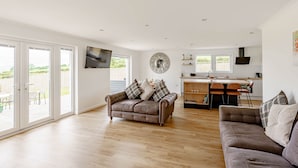 A spacious living area with a large sofa, a dining table, and a kitchen in the background. - Berryrigg Cottage -  a cottage that sleeps 6 guests in 3 bedrooms (Dumfries)
