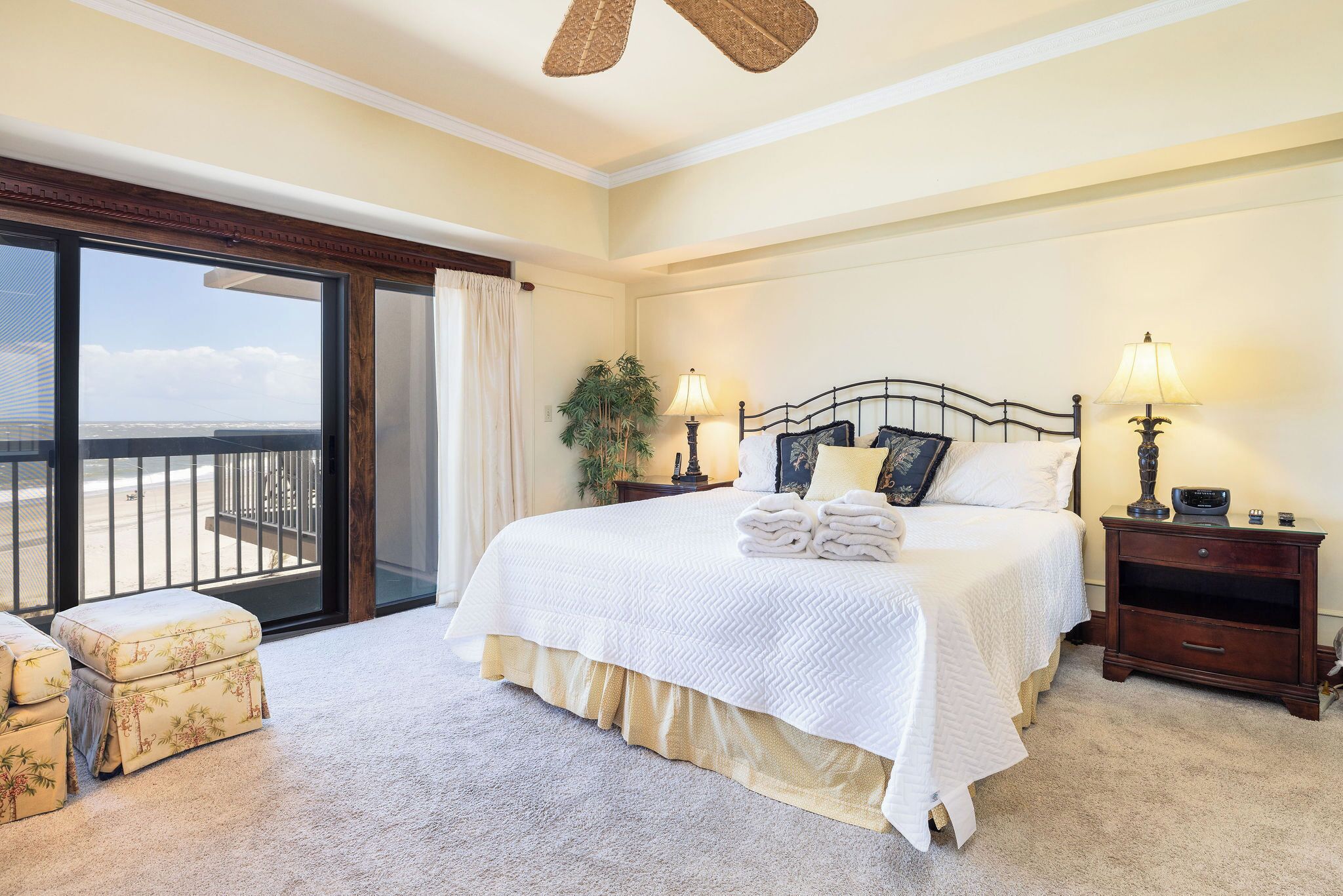A bedroom with a large bed, two bedside lamps, a nightstand, a window with a view, and a ceiling fan.