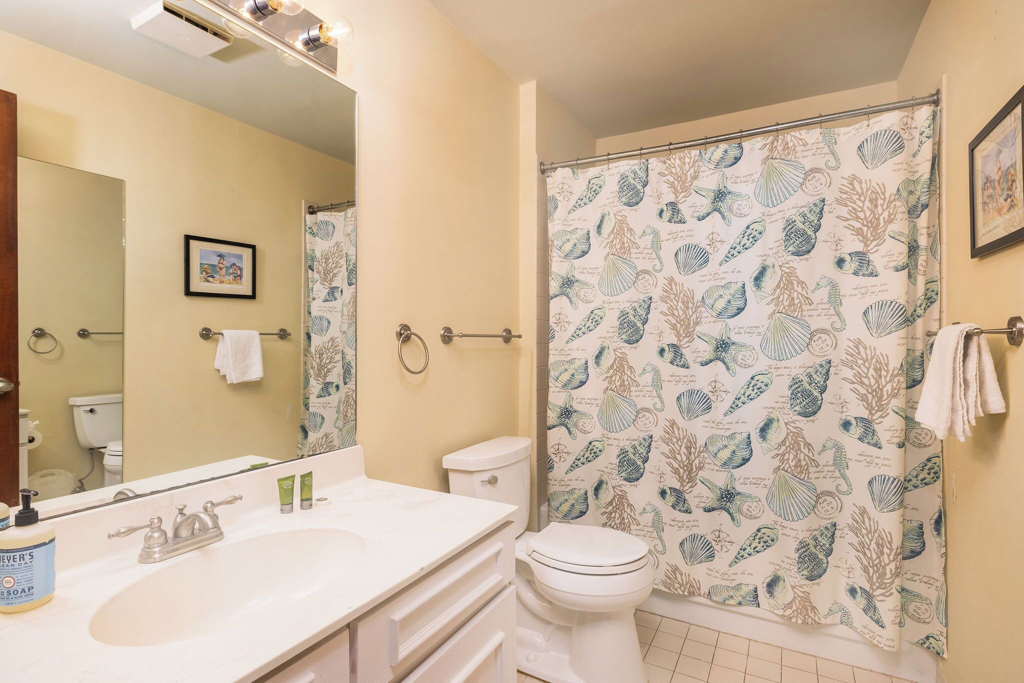 A bathroom with a white sink, a toilet, and a shower curtain with a sea shell pattern.
