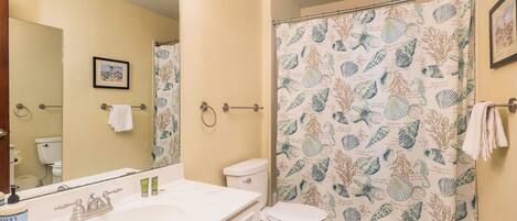 A bathroom with a white sink, a toilet, and a shower curtain with a sea shell pattern.