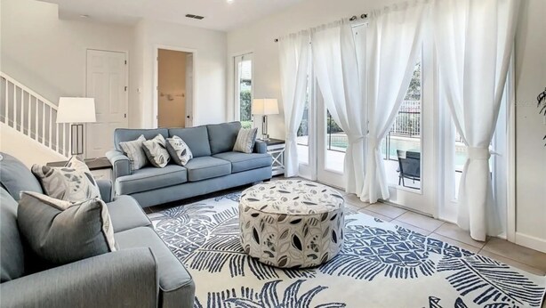 A spacious living room with a blue sofa, a patterned ottoman, and a ceiling fan. - Reunion Resort 3 bed With Private Pool (Kissimmee)