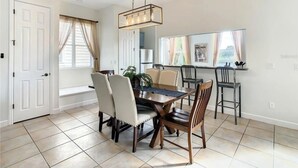 A dining room with a rectangular table, six chairs, a hanging light fixture, and a window with curtains. - Reunion Resort 3 bed With Private Pool (Kissimmee)