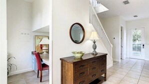 A spacious hallway with a staircase, a wooden dresser with drawers, a red chair, and a wall-mounted mirror. - Reunion Resort 3 bed With Private Pool (Kissimmee)