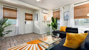 Una sala de estar moderna con una mesa de centro de vidrio, un sofá negro con cojines amarillos y una planta grande.