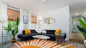 Una sala de estar moderna con un sofá negro, una mesa de centro de vidrio y un tapete estampado naranja.