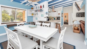 Un vaste espace de vie comprenant une table à manger blanche, des chaises blanches, un ventilateur de plafond et une bibliothèque.