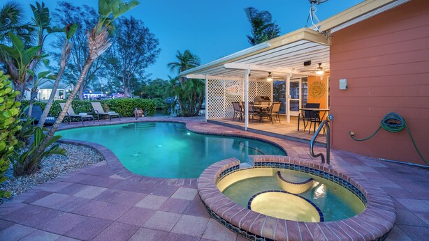 Une piscine avec un jacuzzi, des chaises longues et un patio couvert.