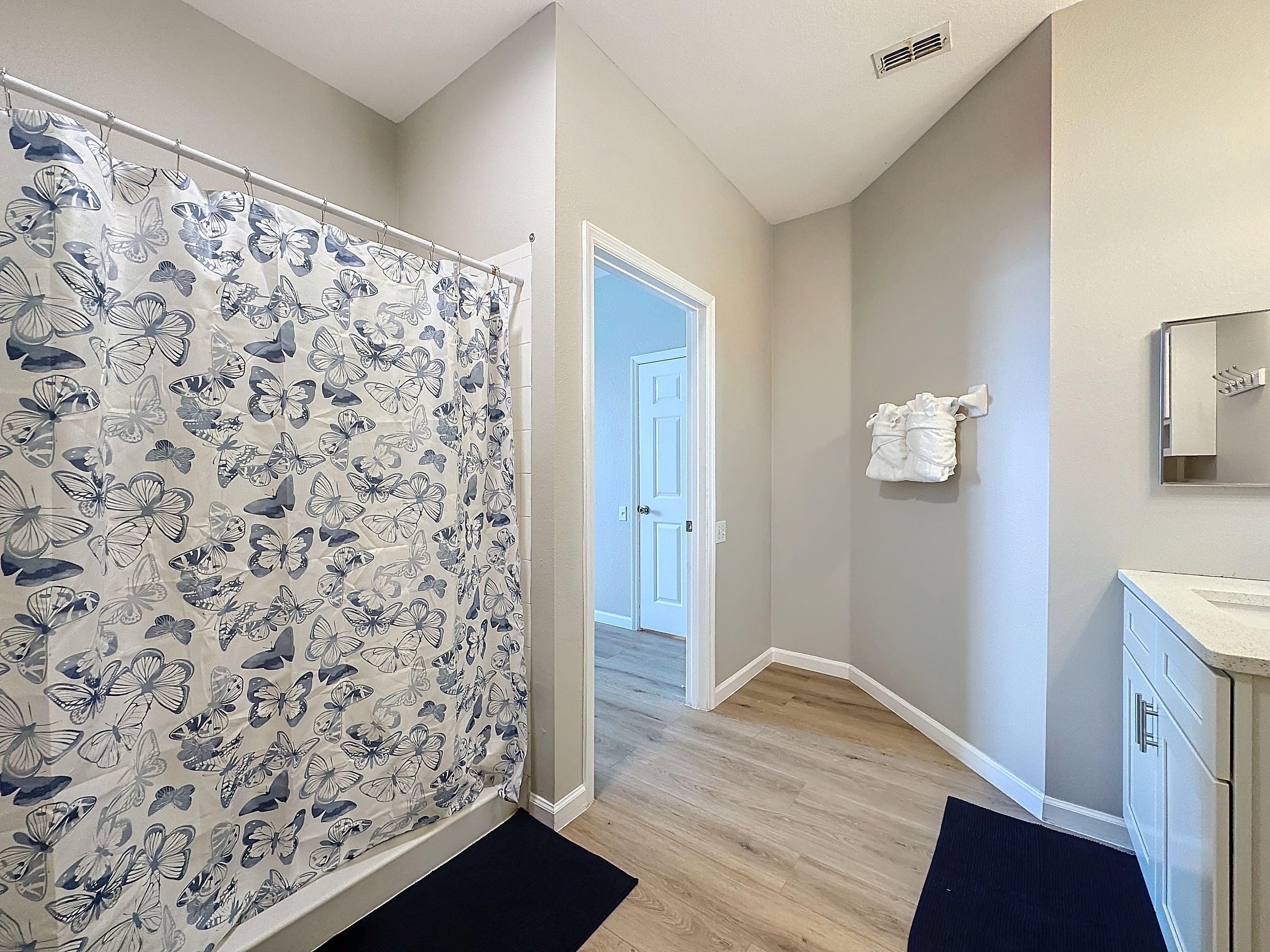 A bathroom with a shower curtain featuring a butterfly pattern, a white door, a towel rack with towels, and a mirror above a sink.