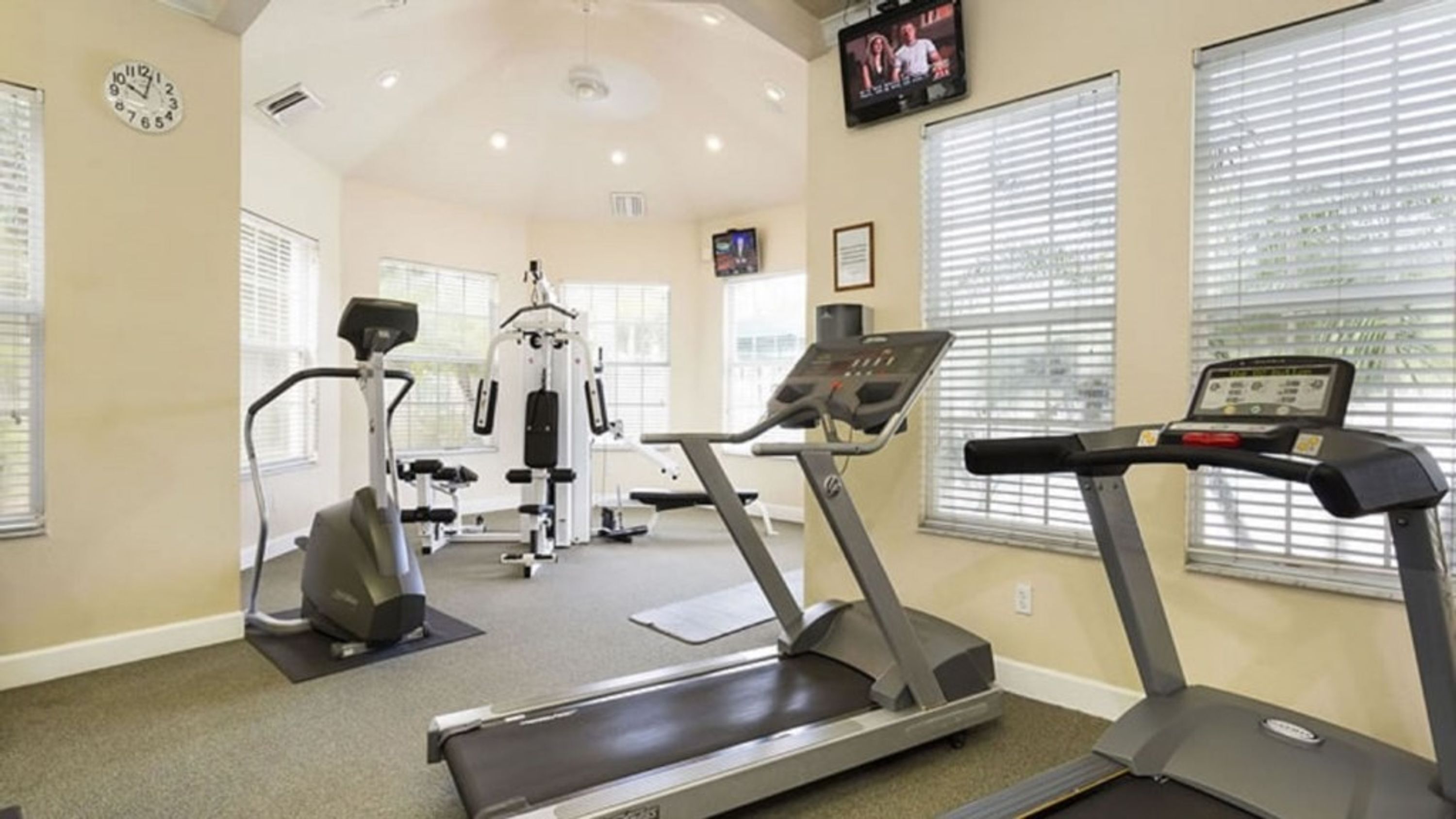 A gym with treadmills, a weight machine, and a wall clock.