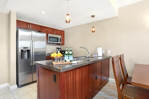 Eine moderne Küche mit einem Edelstahlkühlschrank, einer Mikrowelle und einem Spülbecken. Auf der Arbeitsfläche stehen zwei Bierflaschen.