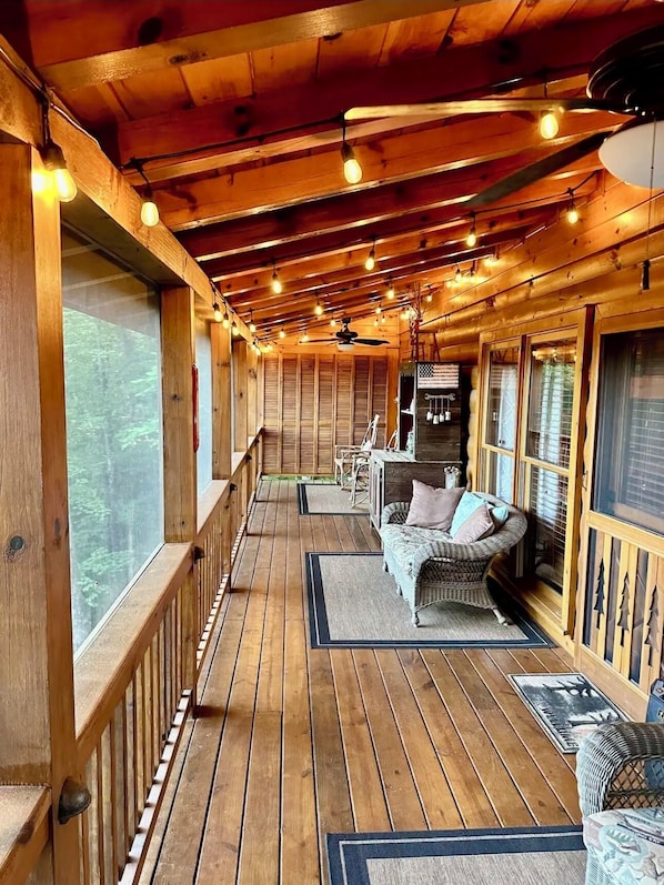 Eine Holzterrasse mit überdachter Sitzgruppe, darunter eine Couch und Stühle sowie ein Esstisch.