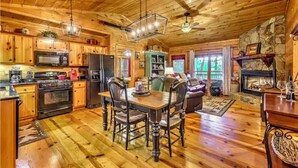 A cozy cabin interior with wooden floors, a dining area with a table and chairs, a kitchen with appliances, and a fireplace. - Cozy Cabin near DT Blue Ridge, GA 🌲Mtn Views💧Hot Tub 🔥Fire Pit 🐶P... (Blue Ridge)