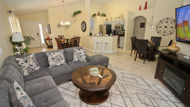 Una sala de estar con un sofá seccional gris, una mesa de centro redonda y una zona de comedor con una cocina al fondo.