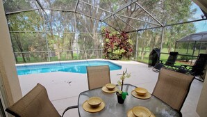 Un espacio al aire libre techado con piscina, sillas y una mesa dispuesta para comer.
