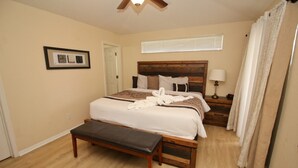 Un dormitorio con una cama grande, un banco de madera, una mesita de noche con lámpara y una ventana con persianas.