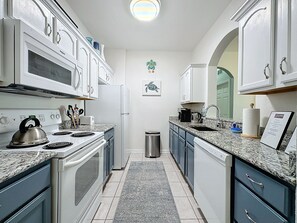 Una cucina moderna con mobili bianchi, un bollitore in acciaio inossidabile, una macchina da caffè e un cestino.