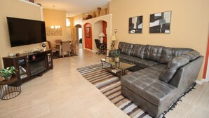 A living room with a large leather sofa, a flat-screen TV, a coffee table, and a striped rug.