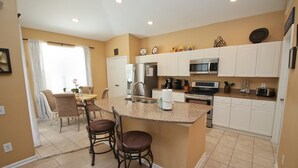A modern kitchen with white cabinets, a granite countertop island, stainless steel appliances, and a dining area with two chairs.