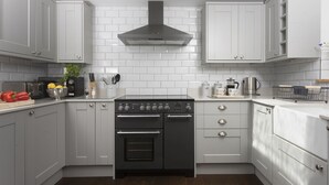 Une cuisine moderne avec des armoires grises, une cuisinière noire et un dosseret de carrelage blanc.