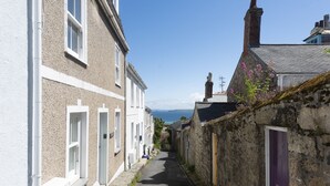 Une rue étroite bordée d’immeubles en pierre, avec une vue dégagée sur la mer et une porte violette sur le côté droit.