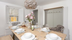 Une salle à manger avec une table en bois mise pour le repas, des assiettes blanches, des verres à vin et une bouteille de vin.